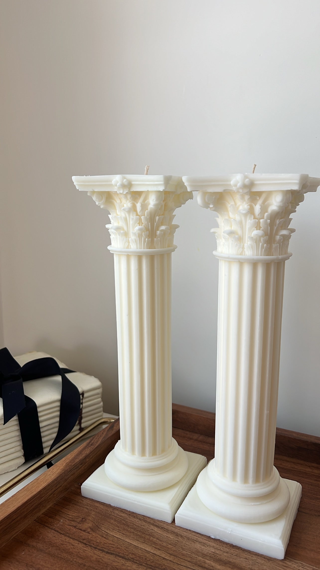 Two white decorative columns on a wooden floor with a neutral background