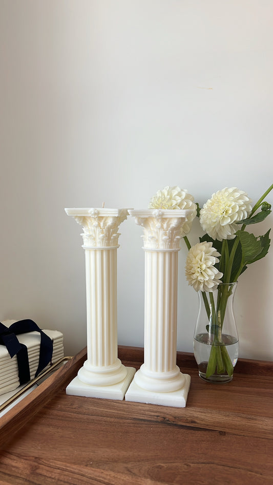 Two white decorative columns on a wooden surface with a vase of flowers in the background.