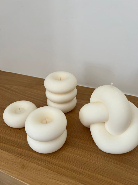 Set of four smooth sculptural candles in modern shapes, arranged on a shelf.