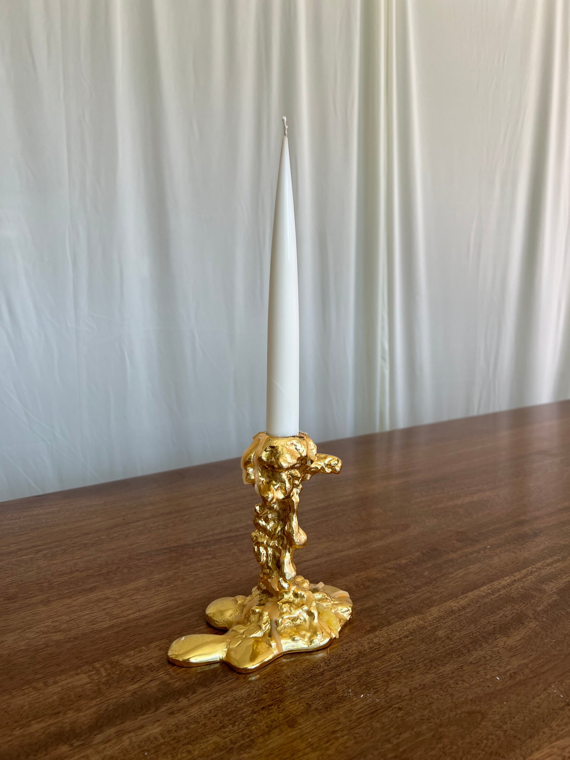 Gold candle holder with a white candle on a wooden surface