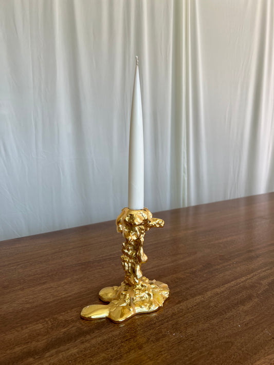 Gold candle holder with a white candle on a wooden surface